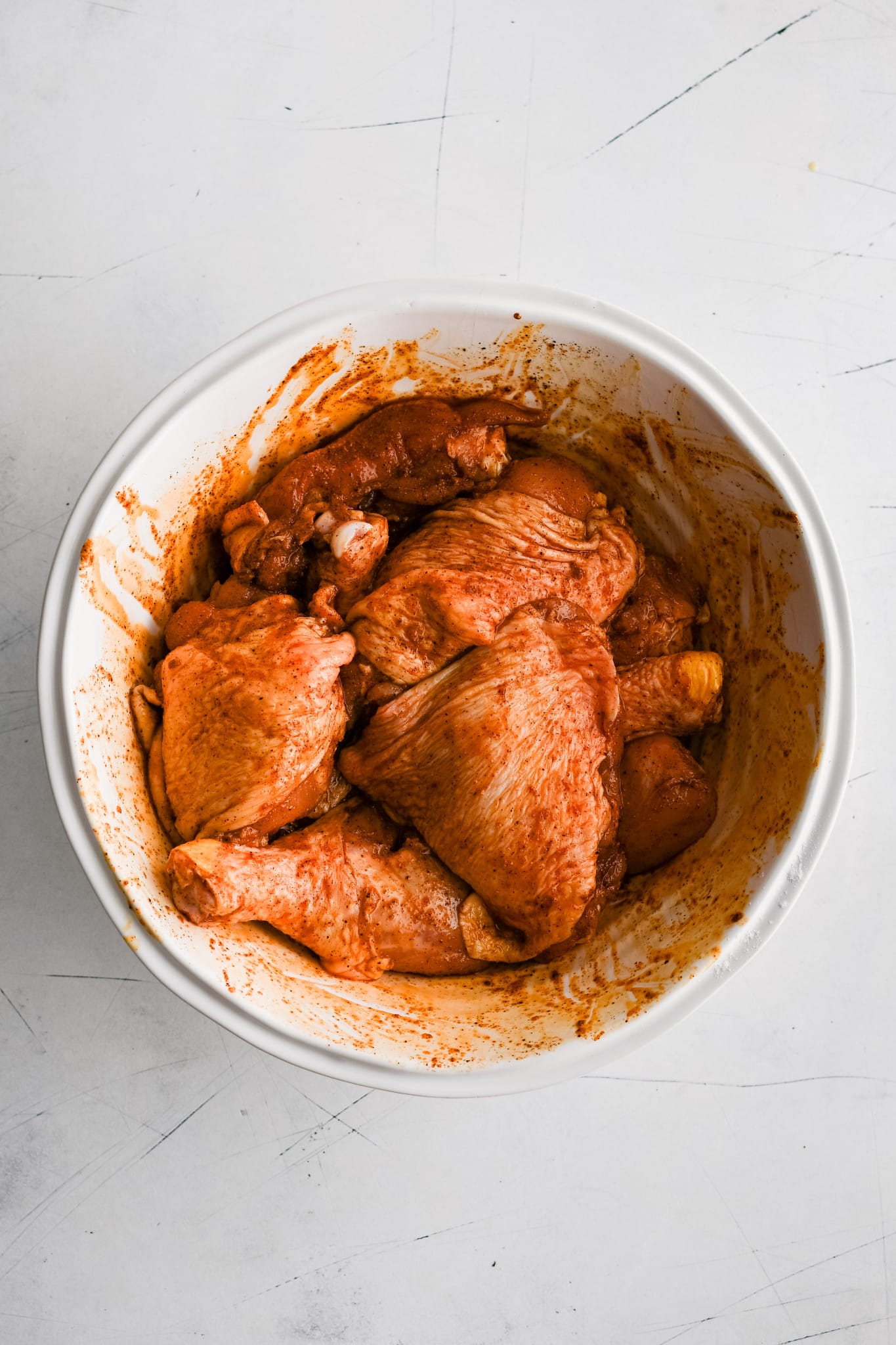 Large white mixing bowl filled with a combination of bone-in skin-on chicken thighs and drumsticks coated evenly in a mixture of baking powder, smoked paprika, garlic powder, onion powder, salt, and black pepper.