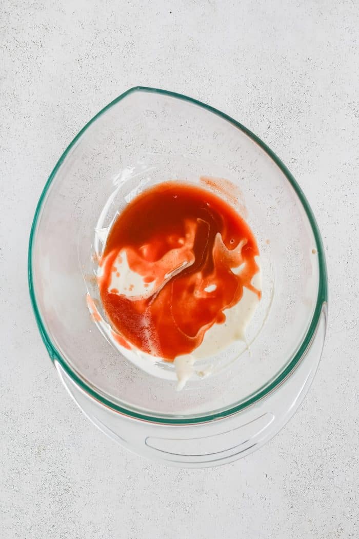 Glass mixing bowl filled with softened cream cheese, ranch dressing, buffalo hot sauce, garlic, and salt,