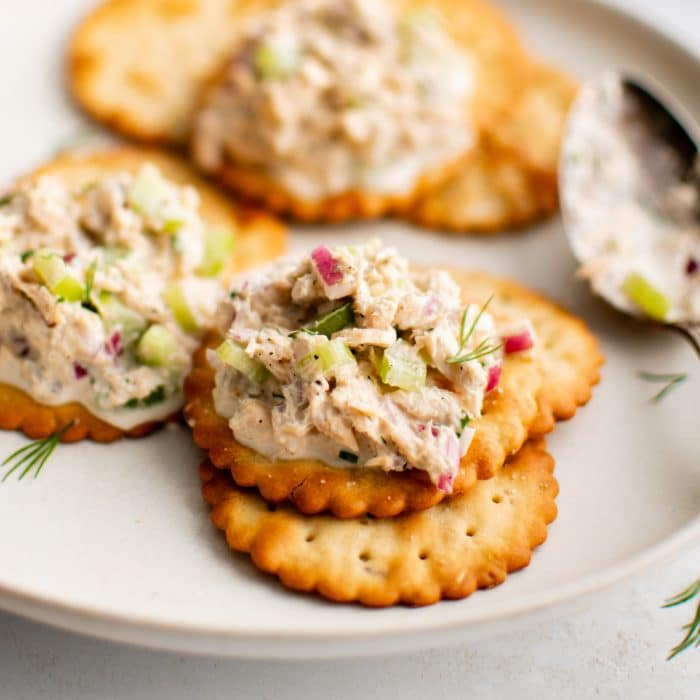 Small plate with golden buttery crackers topped with homemade canned salmon salad and garnished with fresh minced dill.