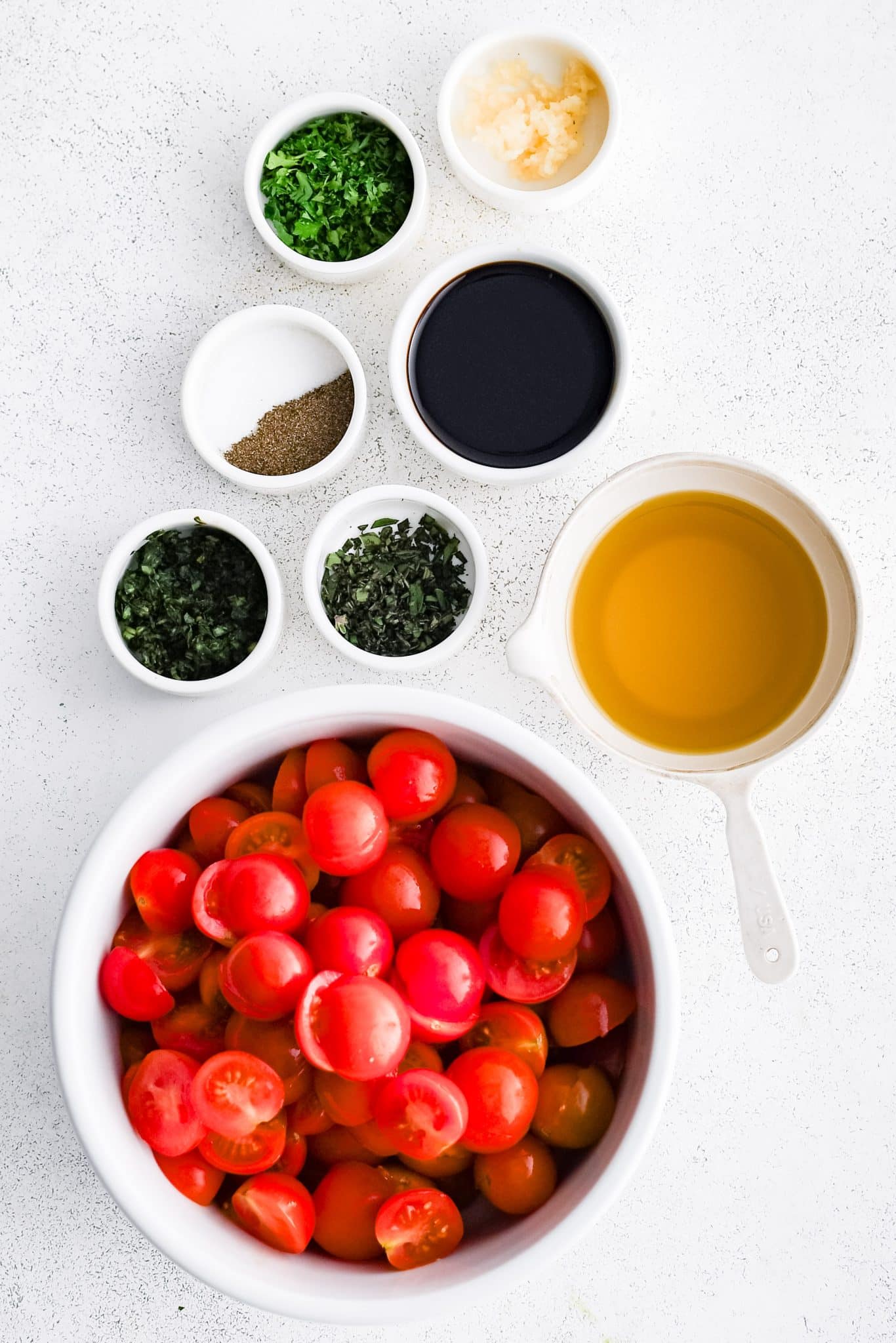 All of the ingredients for Cherry Tomato Salad presented in individual measuring cups and ramekins.