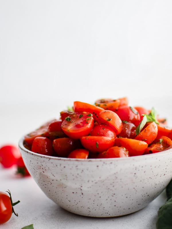 Cherry tomato salad in a rustic-style speckled bowl, styled with basil and whole cherry tomatoes around the base.