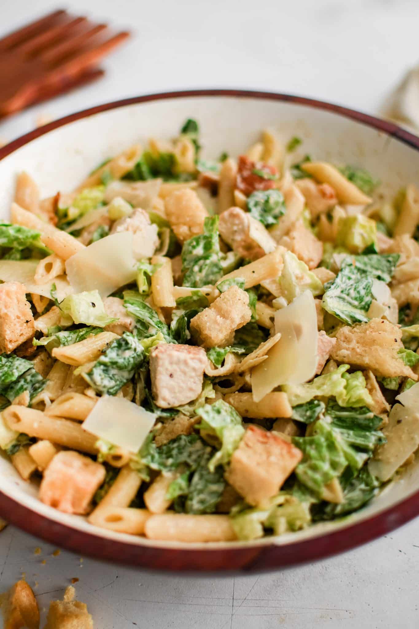 Large salad bowl filled with chicken Caesar pasta salad filled with Romaine lettuce, croutons, chicken, and penne pasta tossed in Caesar salad dressing.