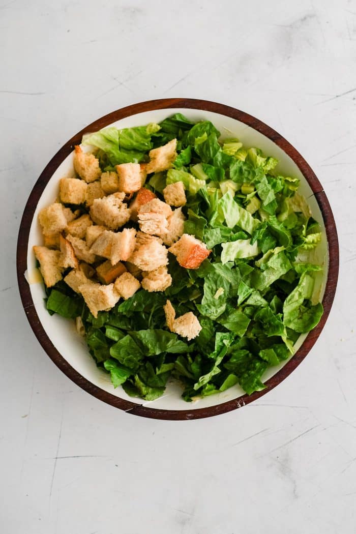 Crunchy croutons and fresh chopped Romaine lettuce added to the bowl filled with chopped cooked chicken, cooked and cooled penne pasta, and parmesan cheese tossed in creamy Caesar salad dressing.