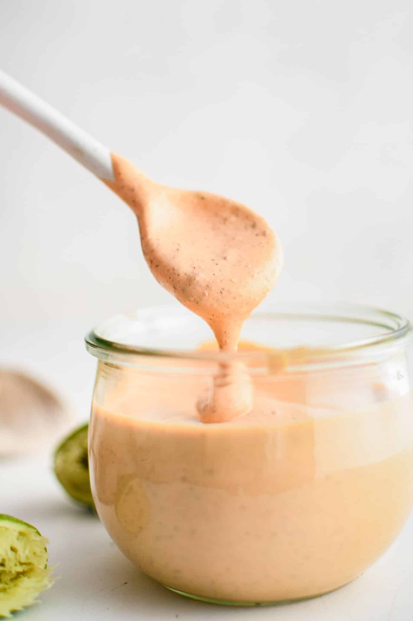 Small white spoon removing a spoonful of chipotle ranch dressing from a small glass jar.