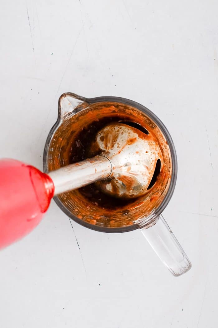 Immersion blender in a glass measuring jar blending together chipotle peppers and adobo sauce with lime juice.