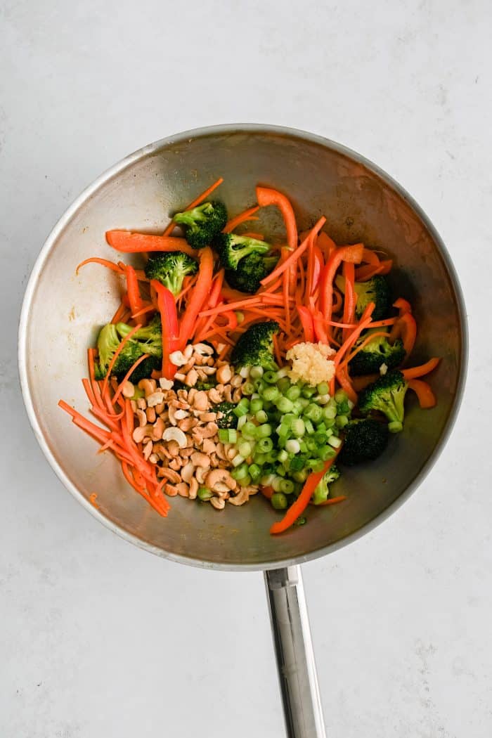 Sliced carrots, broccoli florets, cashews, green onions, and bell pepper in a large wok.