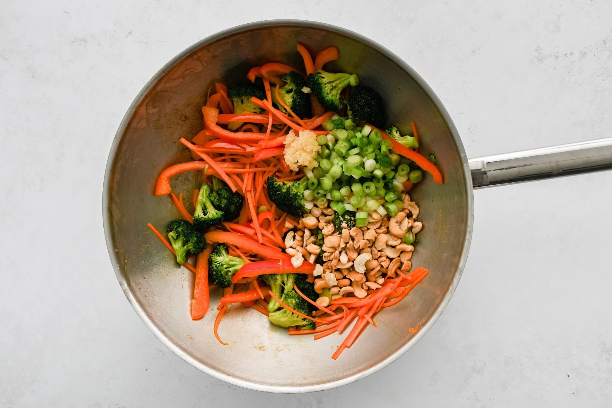 Sliced carrots, broccoli florets, cashews, green onions, and bell pepper in a large wok.