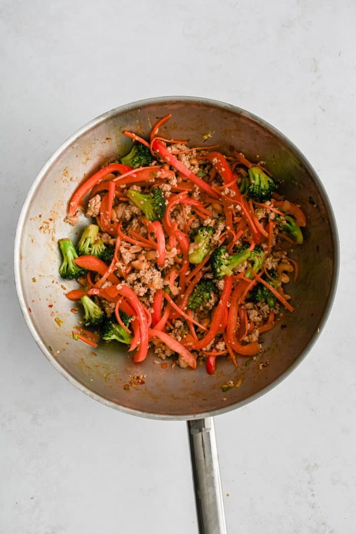 Large wok filled with stir fried carrots, bell pepper, broccoli, green onion, cashews, and ground chicken in a savory stir-fry sauce.