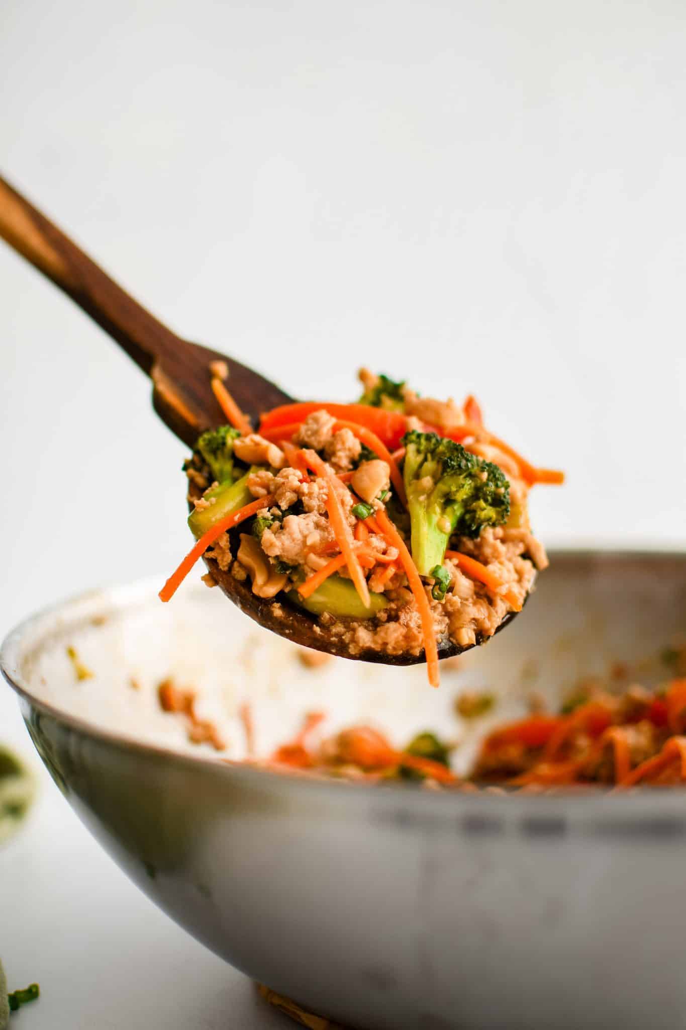 A large wooden serving spoon filled with ground chicken stir fry.