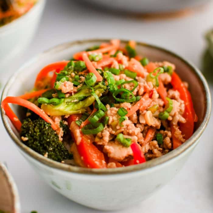 Ground chicken stir fry served in a small bowl on top of a scoop of white rice and garnished with chopped green onions.