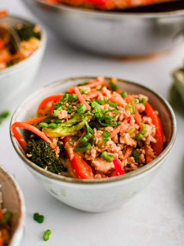 Ground chicken stir fry served in a small bowl on top of a scoop of white rice and garnished with chopped green onions.