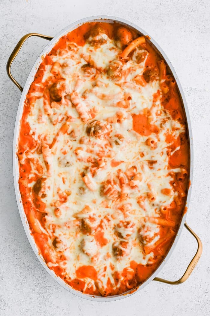 Cheesy dump and bake meatball casserole with ziti pasta and topped with gooey melted mozzarella cheese in a large oval shaped casserole pan.