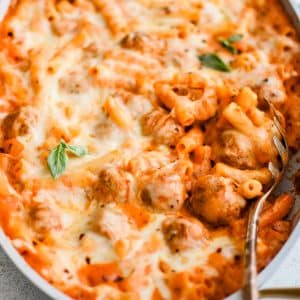 Look inside a large oval-shaped casserole pan filled with thawed meatballs and pasta cooked in a creamy, cheesy marinara sauce and topped with melted mozzarella cheese.