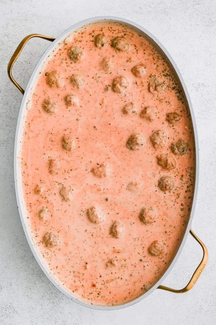Large oval-shaped casserole pan filled with mixed together marinara sauce, chicken broth, thawed meatballs, pasta, heavy cream, Italian seasoning, salt, and pepper.