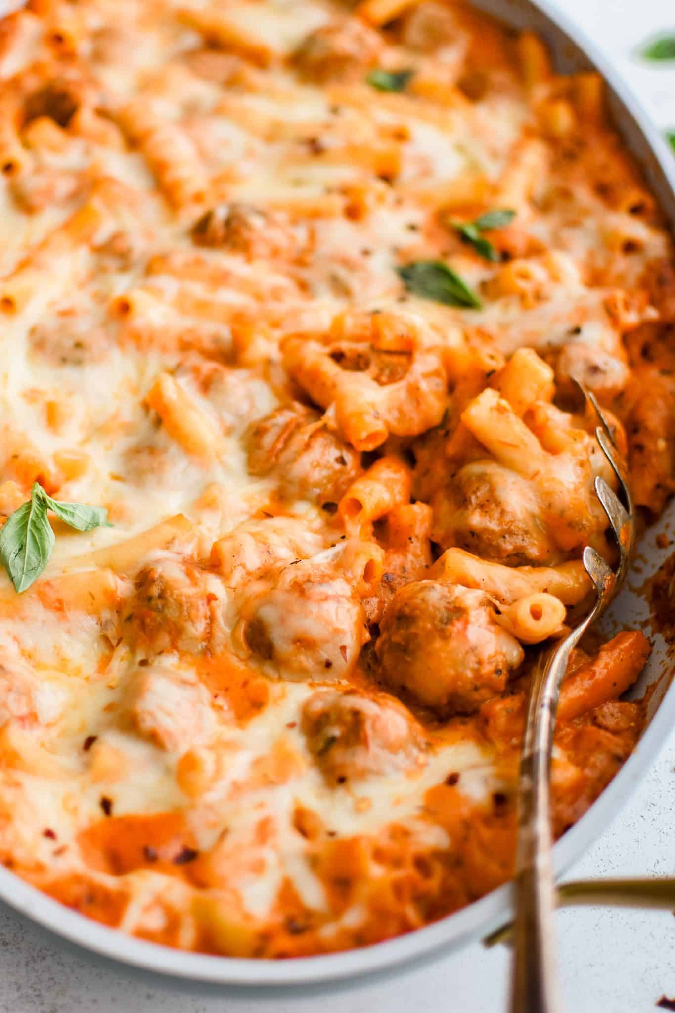 Look inside a large oval-shaped casserole pan filled with thawed meatballs and pasta cooked in a creamy, cheesy marinara sauce and topped with melted mozzarella cheese.