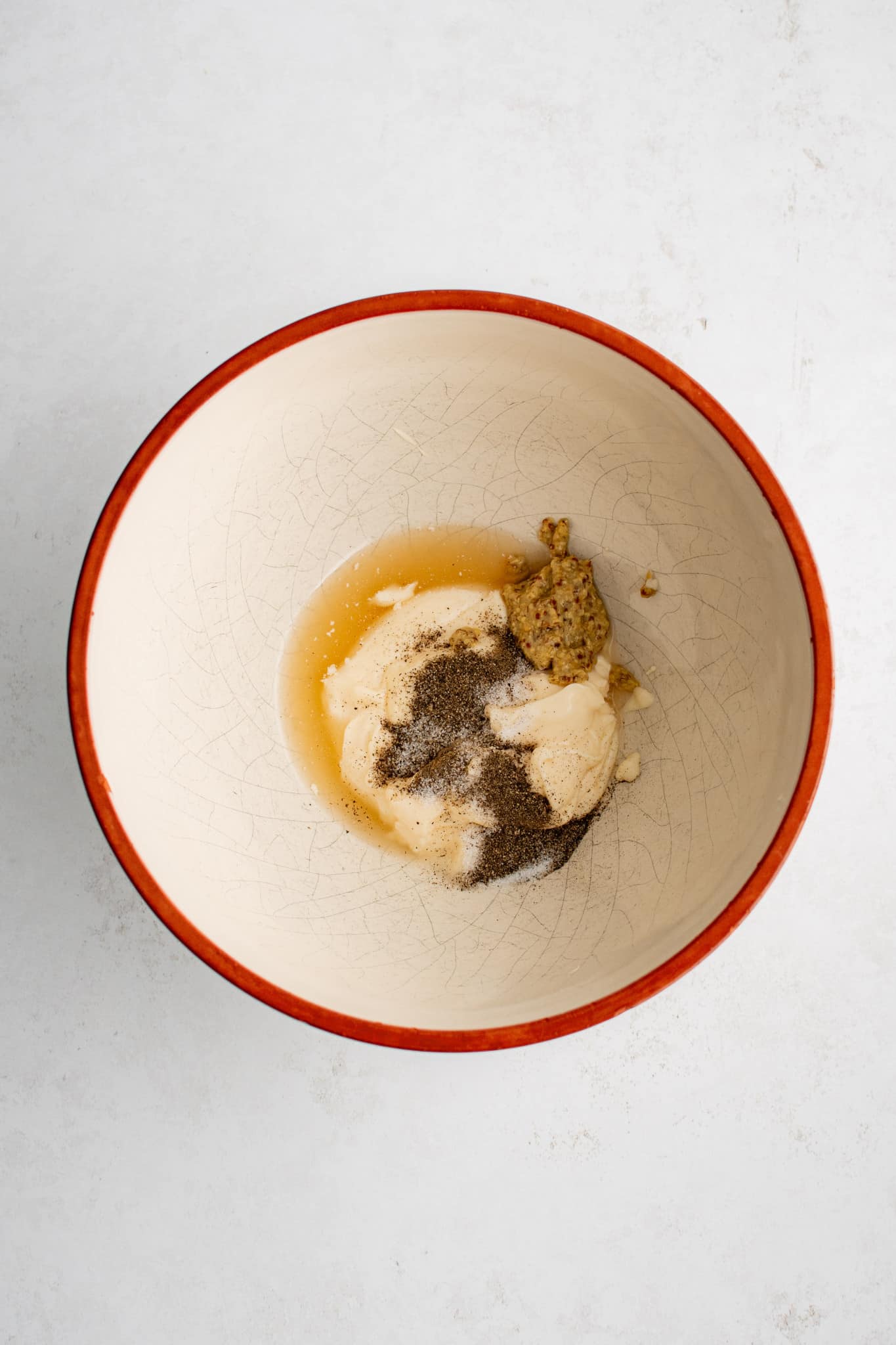 Medium mixing bowl filled with mayonnaise, stone ground mustard, apple cider vinegar, salt, and pepper.