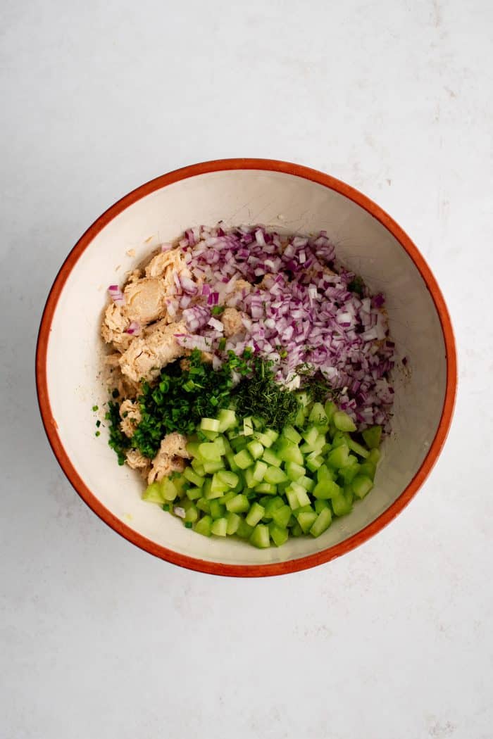 Canned salmon flakes, diced celery, red onion, chives, and fresh dill in a medium mixing bowl.