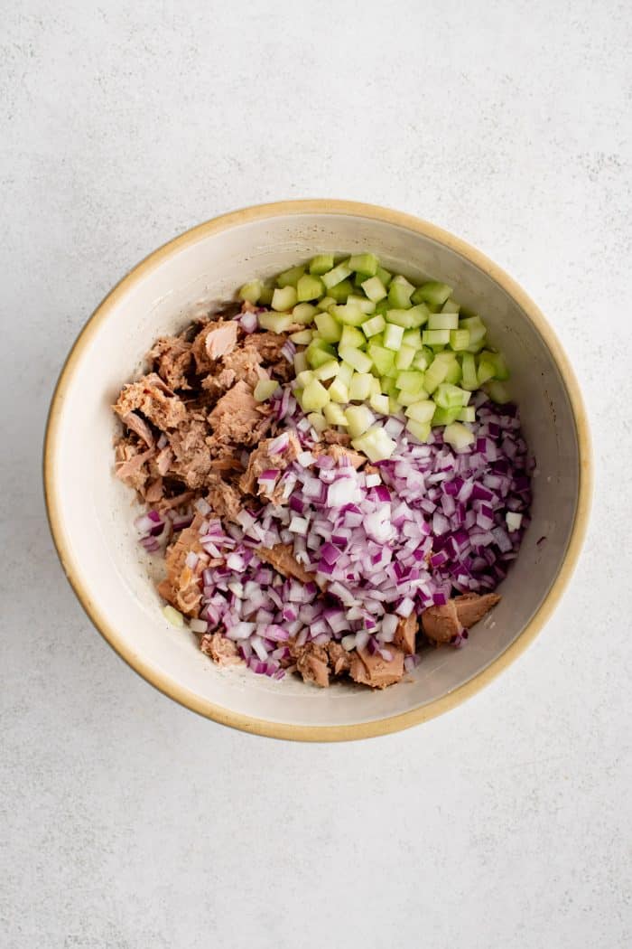 Large mixing bowl filled with drained canned chunk tuna and diced celery and red onion.