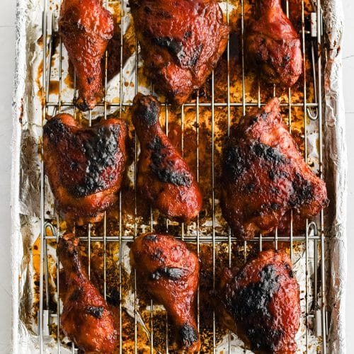 Cooling rack topped with perfectly baked bone-in skin-on BBQ chicken thighs and drumsticks coated in sticky BBQ sauce.