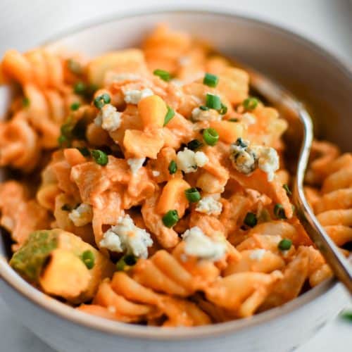 Small serving bowl filled with Buffalo Chicken Pasta Salad garnished with minced chives and crumbled blue cheese.