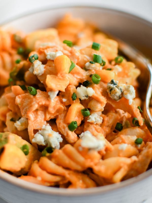 Small serving bowl filled with Buffalo Chicken Pasta Salad garnished with minced chives and crumbled blue cheese.