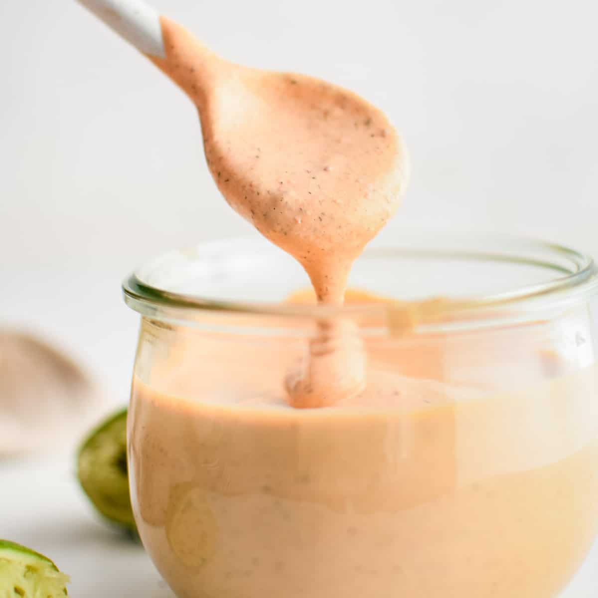 Small white spoon removing a spoonful of chipotle ranch dressing from a small glass jar.