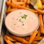Baking sheet filled with crispy sweet potato fries, lemon wedges, and a small glass bowl filled with spicy, creamy, tangy remoulade sauce.