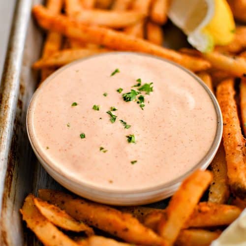 Baking sheet filled with crispy sweet potato fries, lemon wedges, and a small glass bowl filled with spicy, creamy, tangy remoulade sauce.