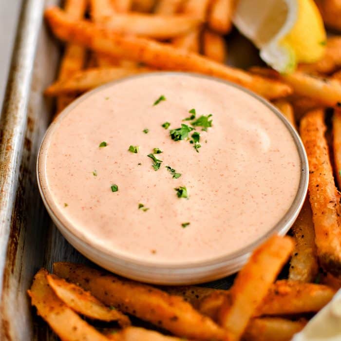 Baking sheet filled with crispy sweet potato fries, lemon wedges, and a small glass bowl filled with spicy, creamy, tangy remoulade sauce.