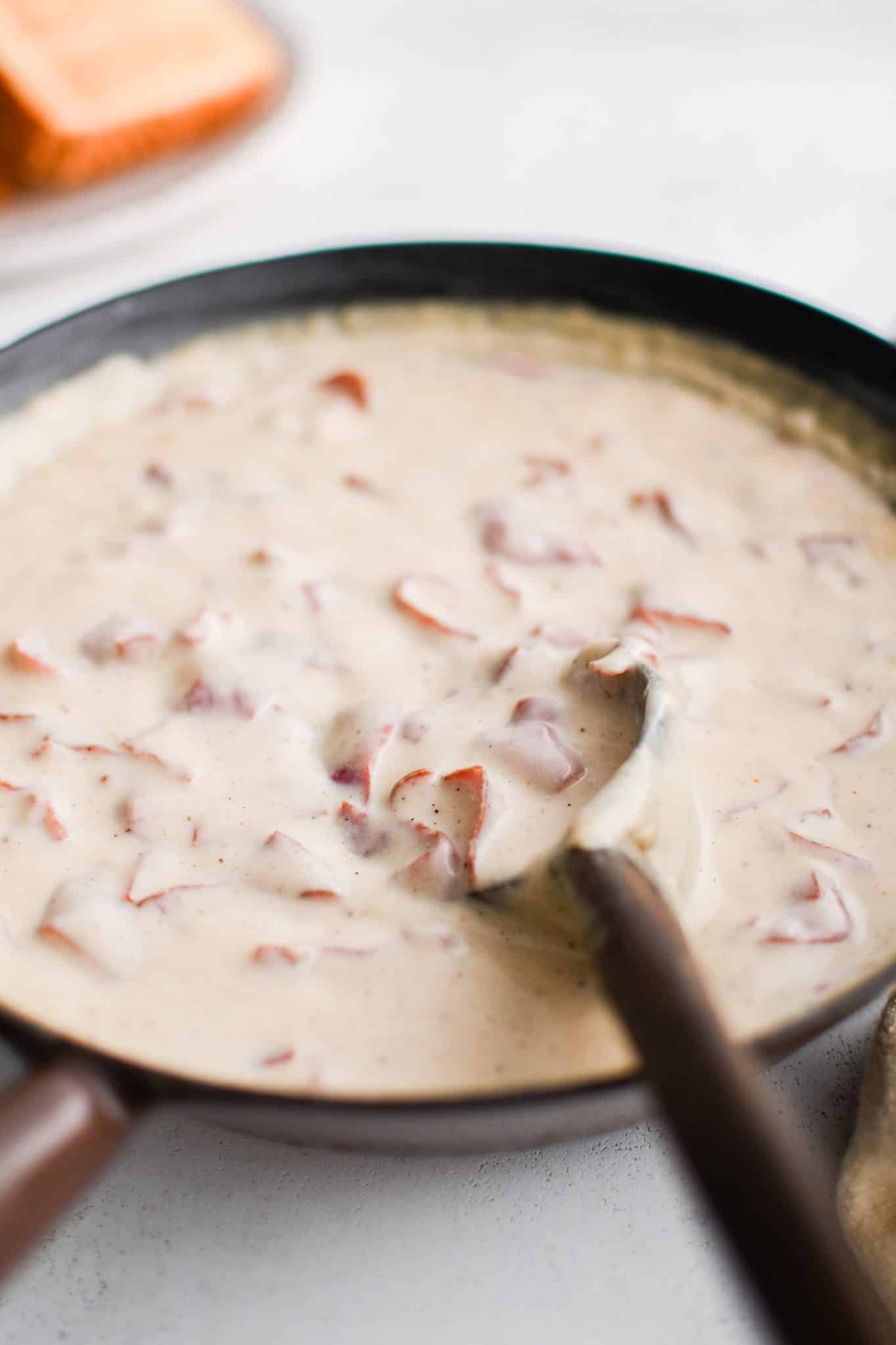 Large cast iron skillet filled with gently simmering chipped beef in a creamy white gravy.