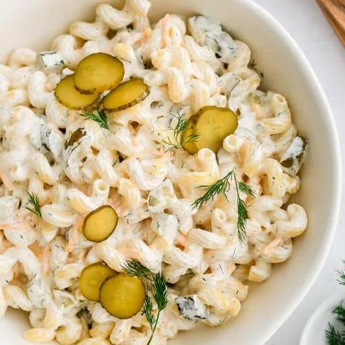 Large white bowl filled with creamy dill pickle pasta salad garnished with sliced dill pickles and fresh dill.