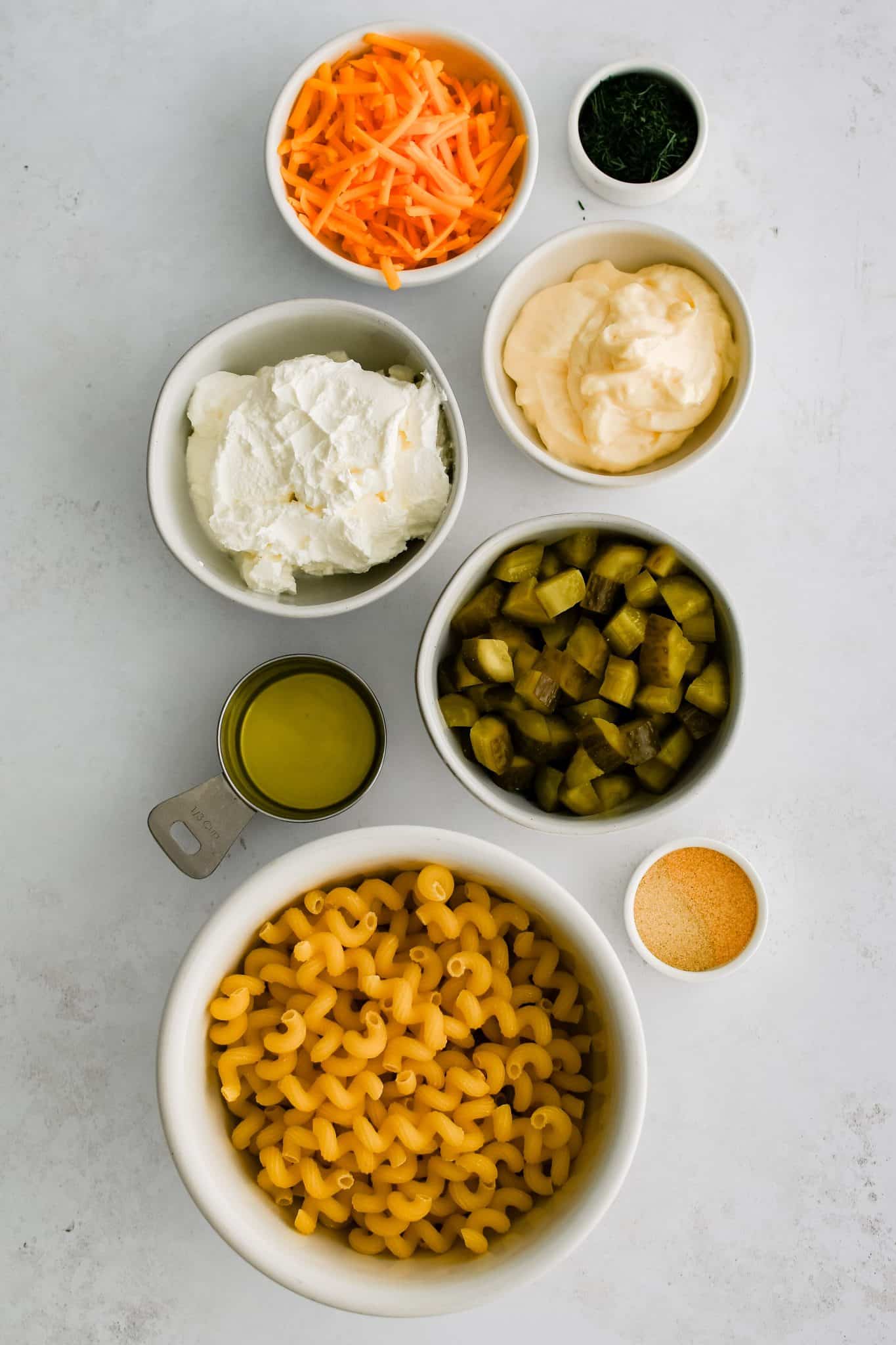 All of the ingredients for the dill pickle pasta salad recipe presented in individual measuring cups and ramekins.