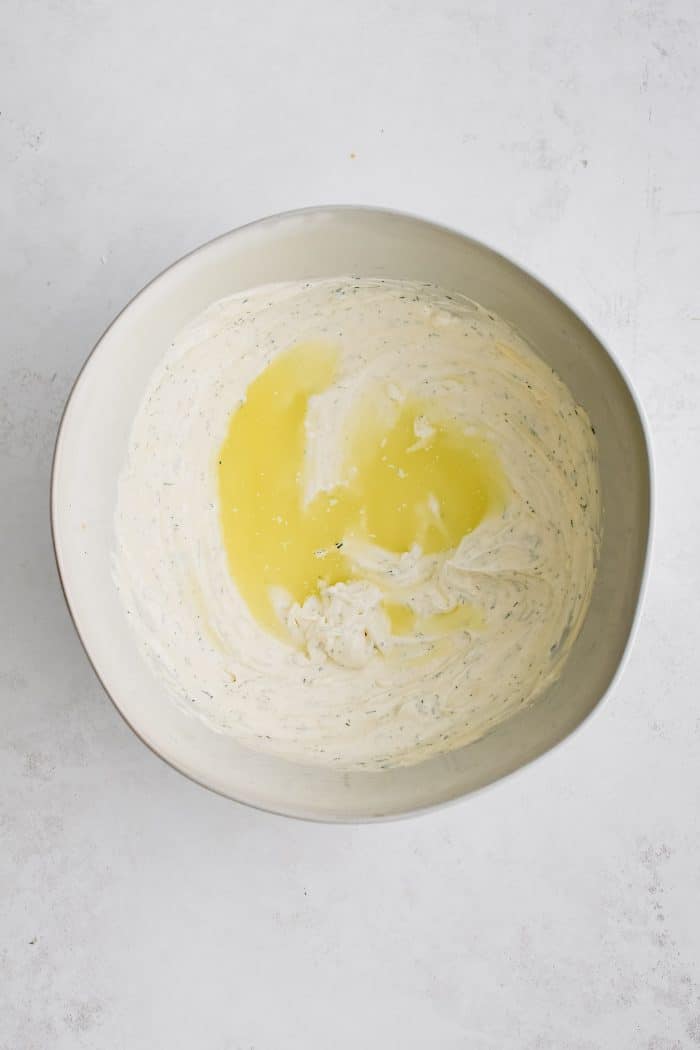 Pickle juice added to a large white mixing bowl filled with creamy mayonnaise and sour cream based dressing.