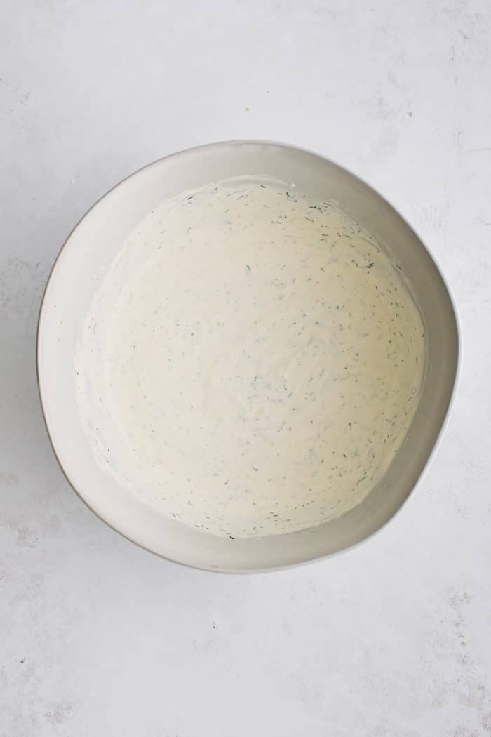 White mixing bowl filled with smooth and creamy dill pickle dressing.
