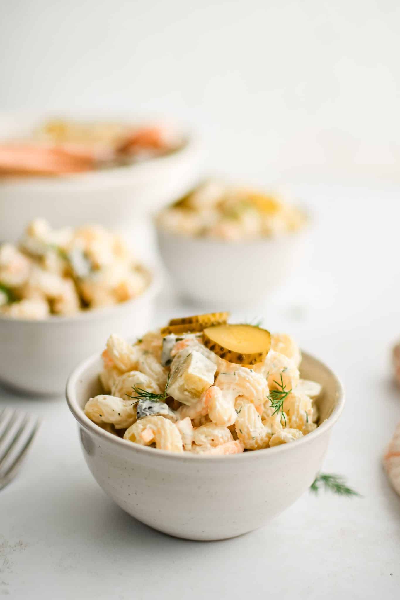 Small white serving bowls filled with creamy dill pickle pasta salad.