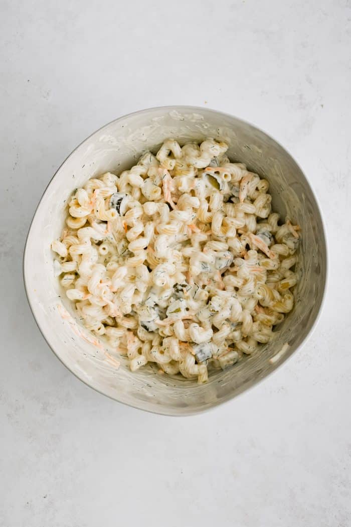 White mixing bowl filled with mixed together creamy dill pickle pasta salad.