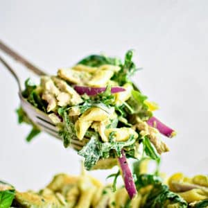 Salad tongs filled with a large serving of green goddess pasta salad and hovering above a large bowl filled with the remaining prepared pasta salad.
