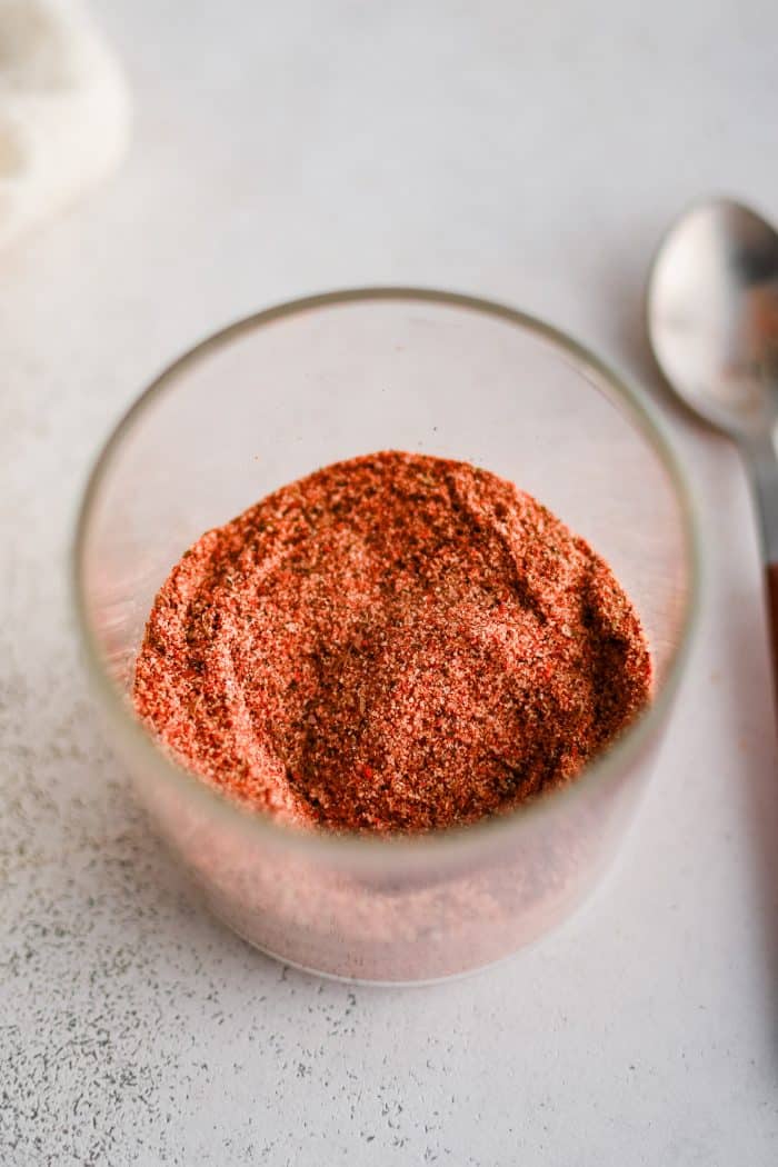 Small clear glass cup filled with mixed together homemade Cajun spice blend.