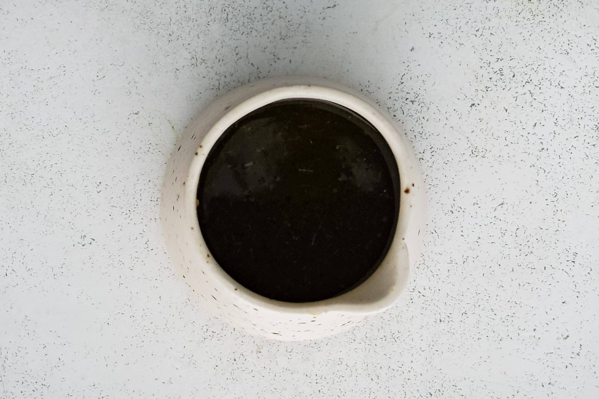 Small white ceramic pitcher filled with dark vinaigrette dressing for La Scala chopped salad, placed on a light textured background.
