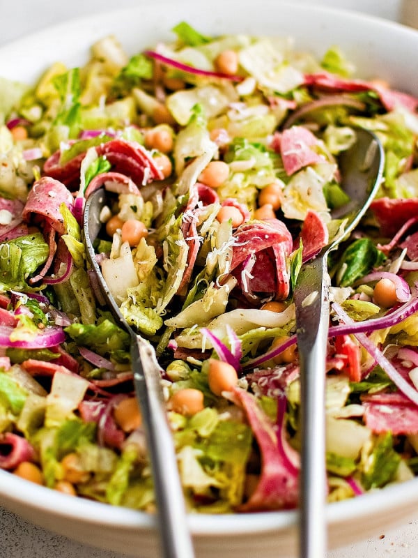 Large white bowl filled with the famous la scala salad that consists of chopped lettuce, salami, chickpeas, mozzarella cheese, and red onion tossed in a tangy dijon vinaigrette.
