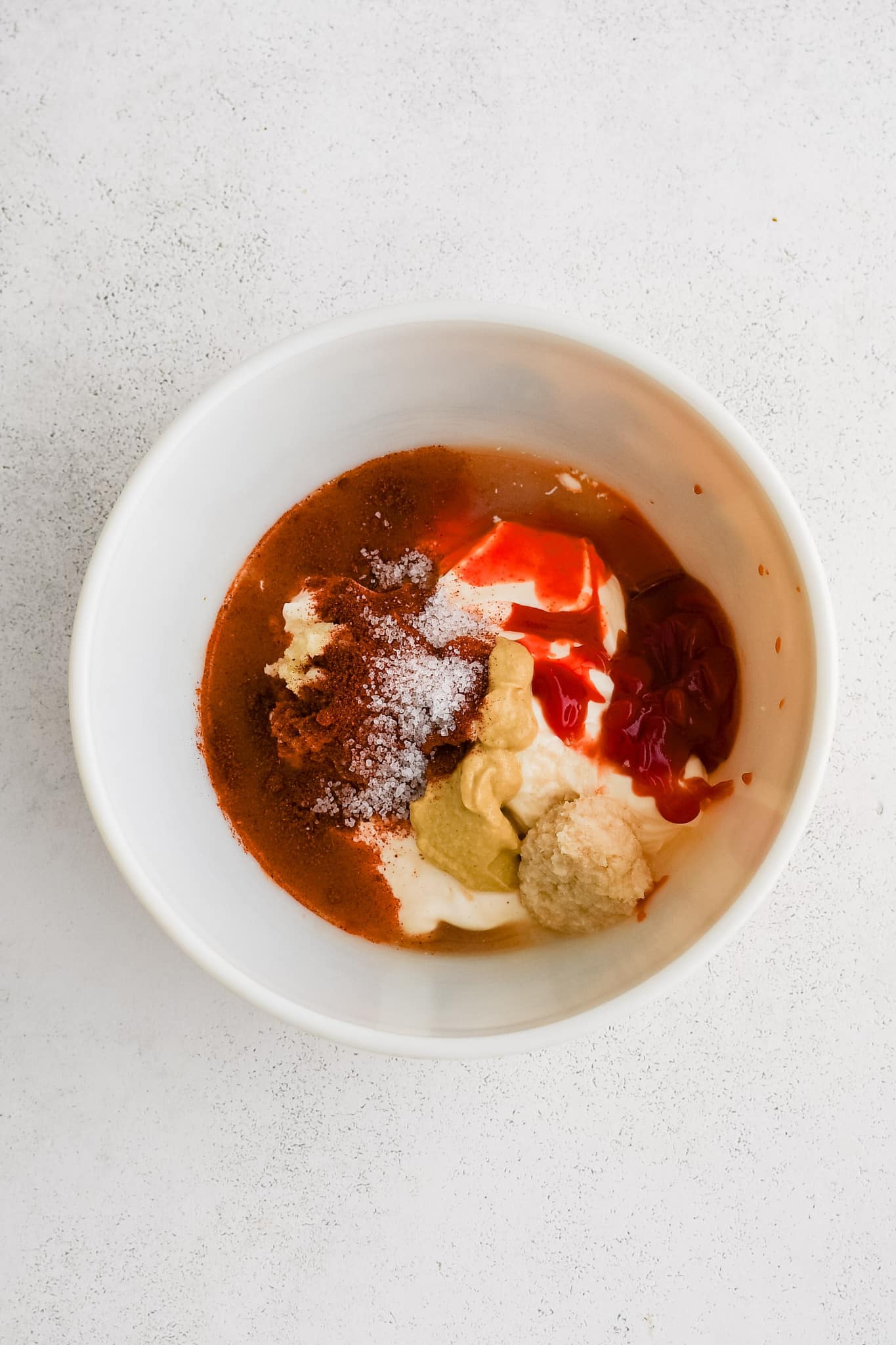Small white bowl filled with mayonnaise, hot sauce, horseradish, lemon juice, ketchup, Dijon, smoked paprika, minced garlic, worcestershire sauce, and salt.