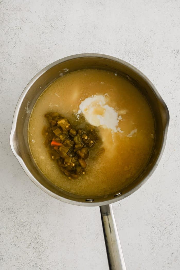 Small saucepan filled with the thickened roux and chicken broth combination, canned green chilies, and the room temperature sour cream mixture.