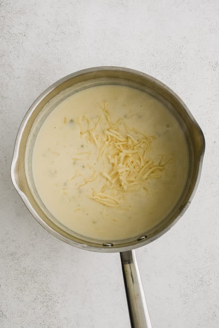 Shredded Monterey Jack cheese added to the small saucepan filled with the combined thickened roux and chicken broth combination, canned green chilies, and the room temperature sour cream mixture.
