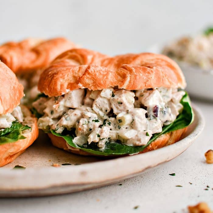 A white plate with three sandwiches made with leftover turkey salad piled between a golden buttery butter croissant with lettuce.