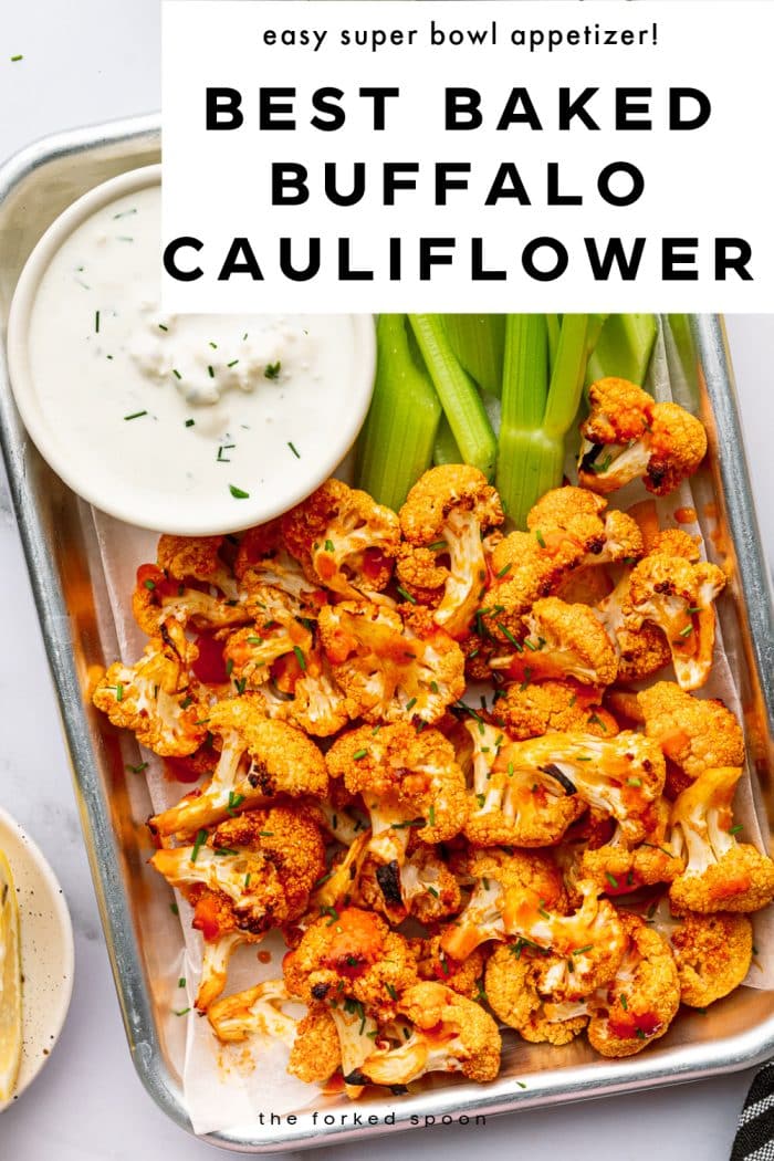 Pinterest pin featuring an overhead photo of baked buffalo cauliflower florets in a small metal tray lined with parchment paper, garnished with chopped green chives and served with bright green celery sticks and a white ramekin of creamy ranch dressing. A white text overlay at the top reads “easy super bowl appetizer!” and bold black text reads “BEST BAKED BUFFALO CAULIFLOWER.” The words “the forked spoon” appear at the bottom of the pin.