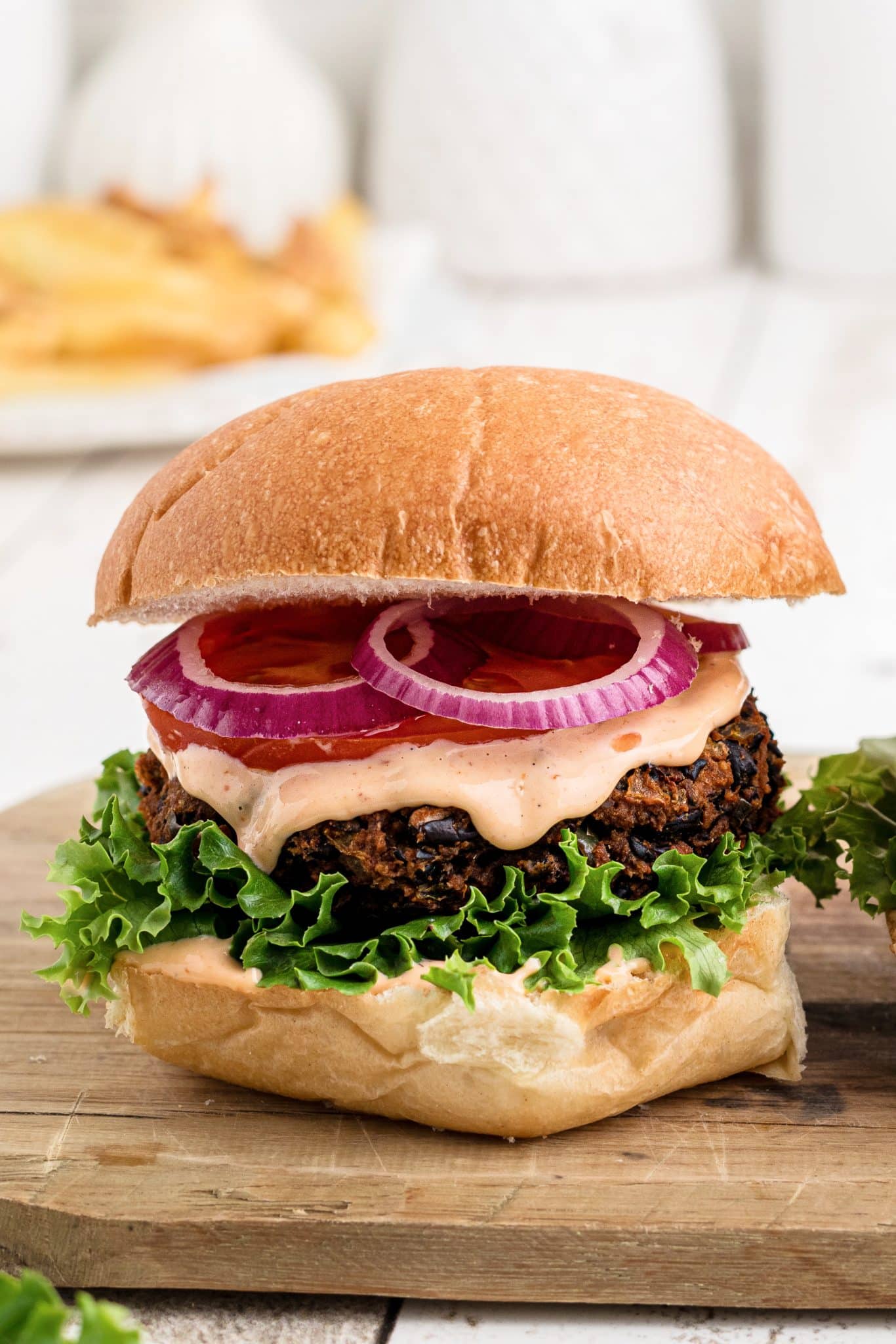 Assembled black bean burger with lettuce, chipotle mayo, sliced tomato, and and sliced red onion on a whole wheat bun.