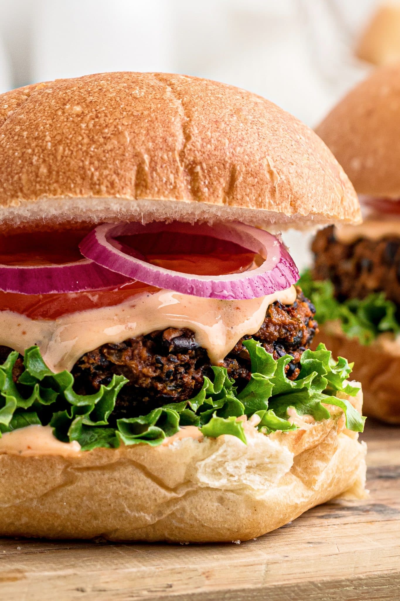 Assembled black bean burger with lettuce, chipotle mayo, sliced tomato, and and sliced red onion on a whole wheat bun.