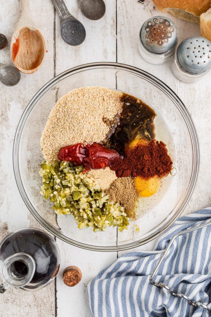 Large glass mixing bowl filled with softened onion and bell pepper, minced garlic, garlic powder, smoked paprika, Chipotle chili powder, cumin, breadcrumbs, eggs, ketchup, Worcestershire Sauce, salt and pepper.