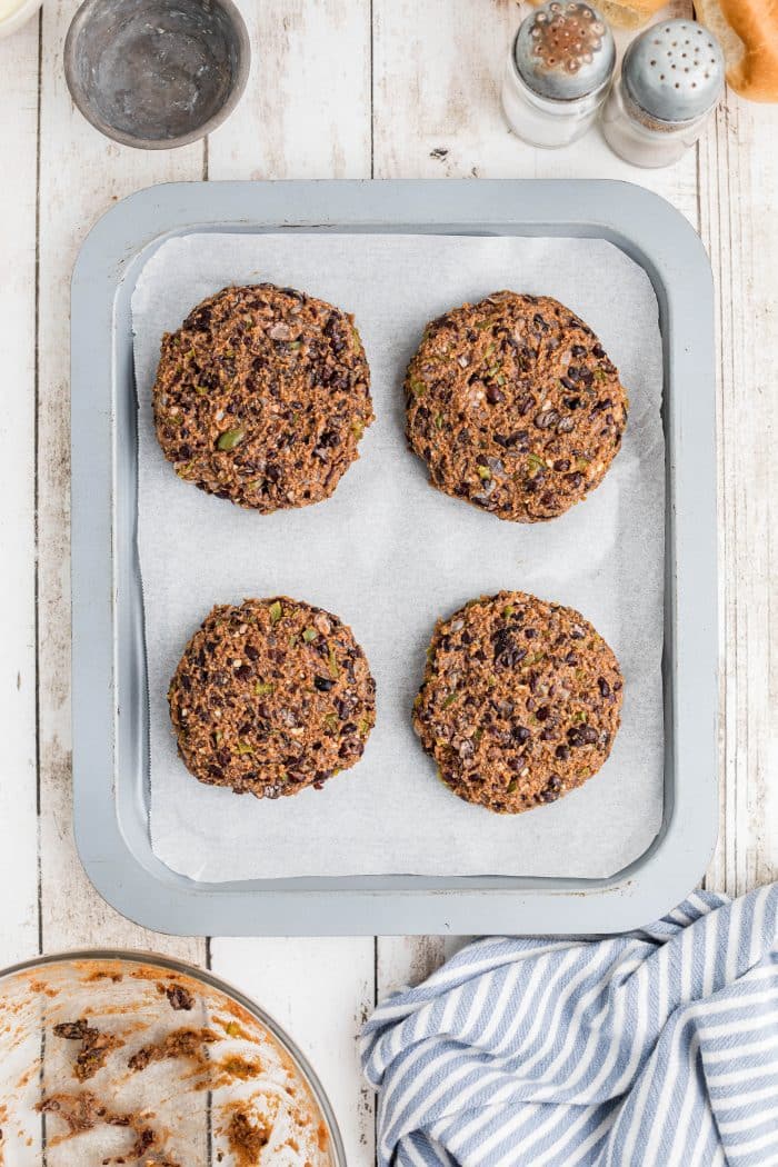 Four perfectly formed black bean burger patties on a baking sheet lined with parchment paper.