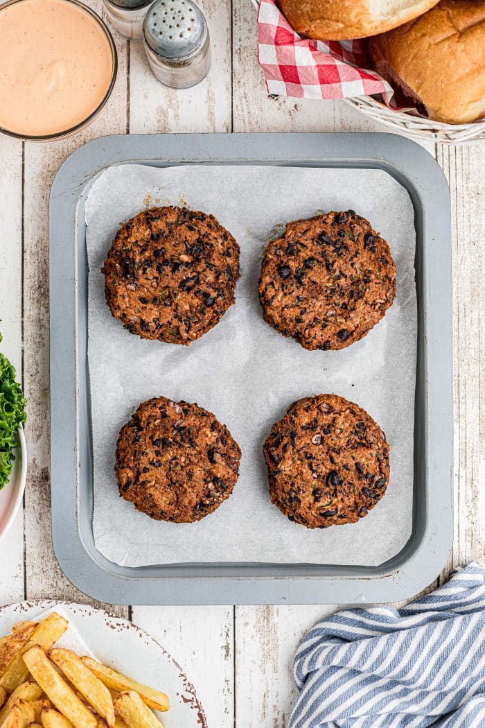 Four perfectly formed cooked black bean burger patties on a baking sheet lined with parchment paper.